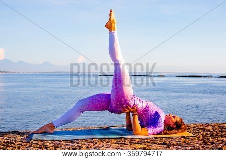 Outdoor Yoga Practice Near The Ocean. Attractive Woman Practicing Variation Of Setu Bandhasana, Shou
