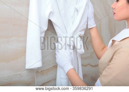The Maid Is Holding A White Terry-cloth Robe. The Concept Of Development Of Hotel Business. A Copy O