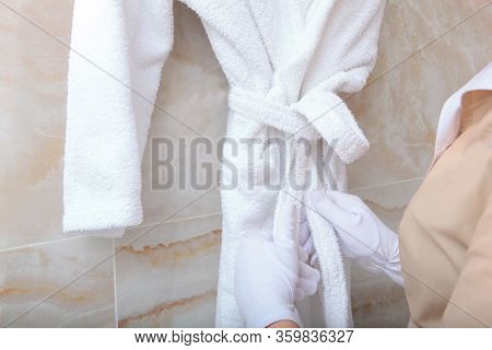 The White-gloved Hands Of The Maid Tie The Belt On The Dressing Gown In The Bathroom.. The Concept O