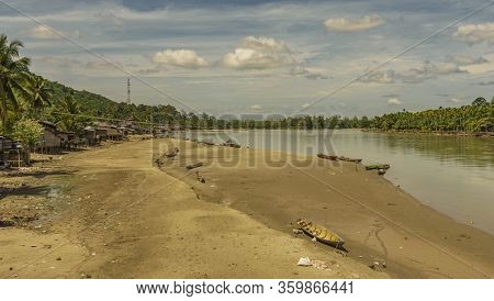 Simple Village Scene Houses On Stilts Nexto To Big Dirty River Surrounded By Jungle And Mountains. A
