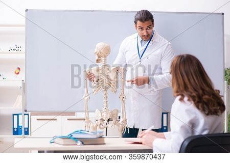 Young male teacher doctor, skeleton and female student in the cl