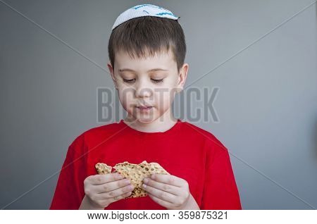 Cute Caucasian Child In A White Kippah Cap Eating Shmura Matzo, A Piece Of Traditional Jewish Unleav