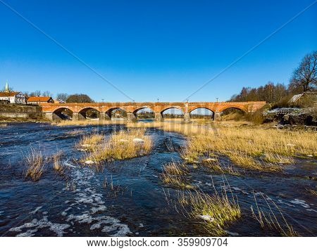 Beautiful Sunny View Of River Wenta Flowing Towards Old Brick Bridge In Old Historic Countryside Cit