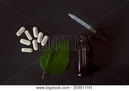 A Glass Brown Bottle Of Liquid And Colorful Tablets Are Placed On A Black Background In The Dark Wit