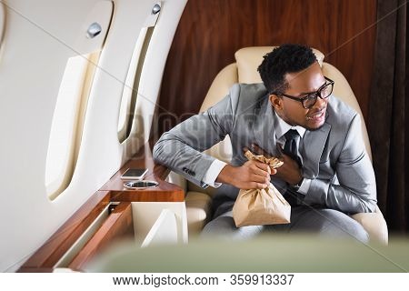 Nervous African American Businessman Holding Paper Bag While Having Panic Attack During Flight On Pr