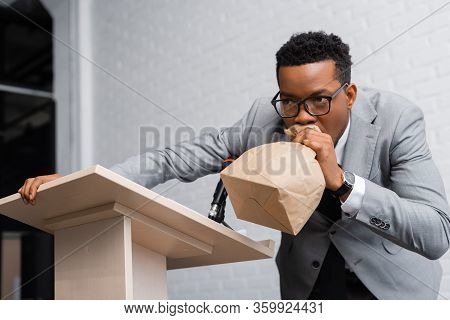 Stressed African American Speaker Breathing With Paper Bag And Having Panic Attack On Business Confe