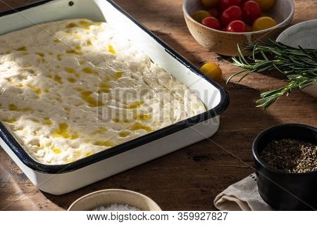 Cooking Focaccia Bread Or Pizza. Raw Focaccia With Ingredients On The Table, Tomatoes, Olives, Rosem