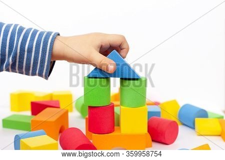 A Child Builds A Pyramid Of Cubes On A White Background. The Boy's Hand Holds A Cube.