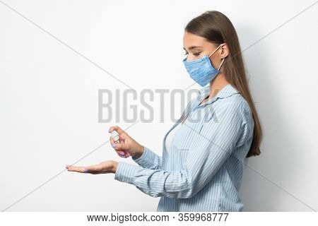 Coronavirus Hygiene. Woman In Mask Using Medical Sanitizer Spray Sterilizing Hands Standing Over Whi