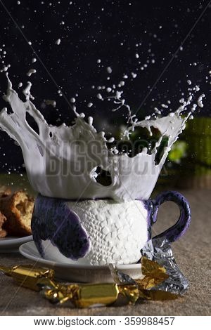 Blue Ceramic Cup With Splashes Of Milk And Candy On Black Background