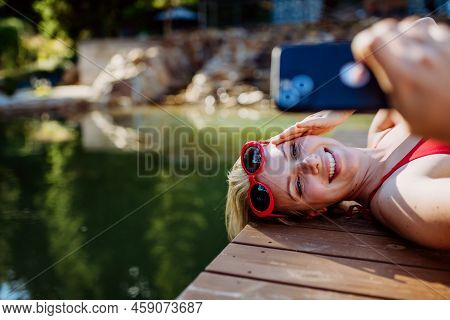 Rlaxed Woman Relaxing On The Pier, Lying And Taking Selfie Near The Natural Lake In Summer