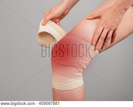 Woman Wrapping Elastic Bandage Around Painful Knee To Relieve Pain Or Prevent Injury. Female Sufferi