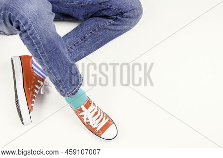 Kid Wearing Different Pair Of Socks. Child Foots In Mismatched Socks And Red Sneakers Sitting On Whi
