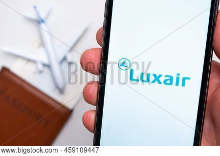 Luxair Airline Application On The Smartphone Screen Mans Hand. A White Toy Airplane And A Passport A