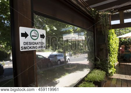 Designated Smoking Area Sign Pointing To Open Garden Area. Hotel Smoking Policies Concept