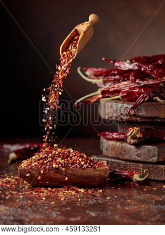 Chilli Flakes Are Poured Into A Wooden Dish. Chilli Flakes And Dried Chili Peppers On A Brown Backgr