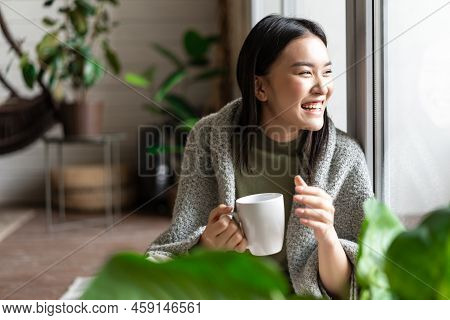 Happy Asian Woman Drinking Morning Coffee And Laughing, Looking Outsie Window Cheerful