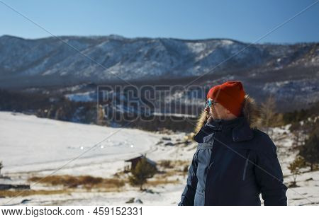 Traveller Man In A Blue Winter Jacket Ad Red Cap In The Woods. Sandy Bay, Baikal Lake, Winter Time. 