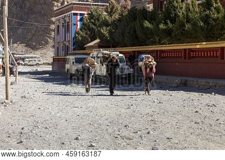 Jomsom, Nepal - November 23, 2016: Three Porters Carrying Heavy Loads. Three Nepalese Men Walking Do