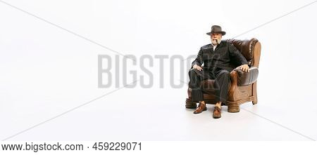 Portrait Of Stylish Senior Man In Retro Style Clothes, Vintage Outfit Sitting At Armchair Isolated O