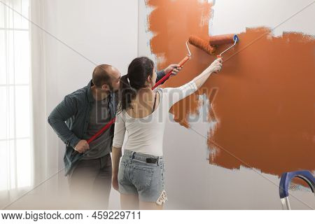 Family Using Orange Color Paint On Walls To Redecorate Apartment Room During Interior Design Renovat