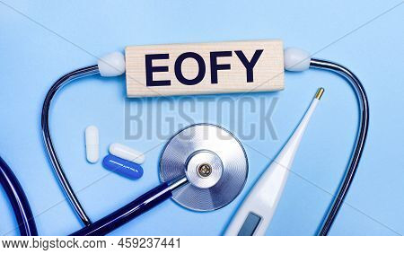 On A Light Gray Background, A Stethoscope, An Electronic Thermometer, Pills, A Wooden Block With The