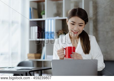 An Asian Female Employee Sits With A Red Coffee Mug In The Startup's Marketing Department Office, Sh