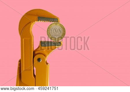 100 Kazakhstani Tenge Held In An Orange Plumber Wrench On A Pink Background. Reverse Side Of The Coi