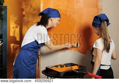 Cheerful People Using Brush To Paint Wall With Orange Color, Home Interior Redecoration. Woman With 