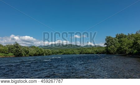 Ripples And Foam Are Visible On The Surface Of The River. Lush Green Vegetation On The Banks. Mounta