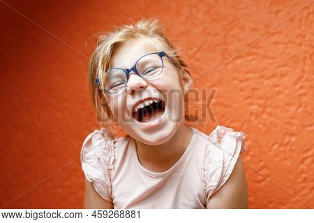 Happy Little Girl In Glasses On Orange Background. Lauging And Smiling Preschool Child, World Smile 