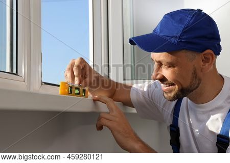 Worker Using Bubble Level After Plastic Window Installation Indoors