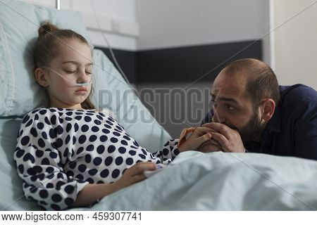 Unwell Sick Kid Sleeping While Uneasy Parent Sitting Beside Her Inside Healthcare Facility. Worried 