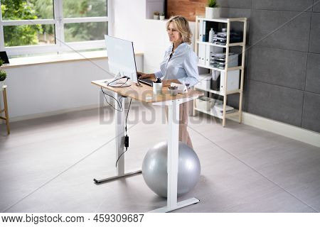 Woman Using Adjustable Height Standing Desk In Office For Good Posture
