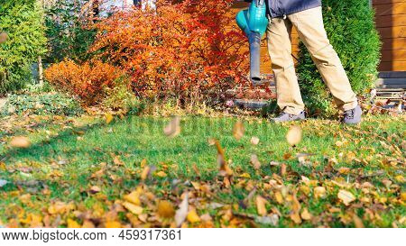 An Electric Blower Removes Leaves From The Lawn With A Powerful Jet Of Air. Fallen Leaves Fly In The