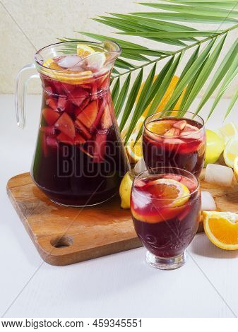 Pitcher And Glasses With Sangria. Orange Slices, Palm Branch. Composition On A Light Background.