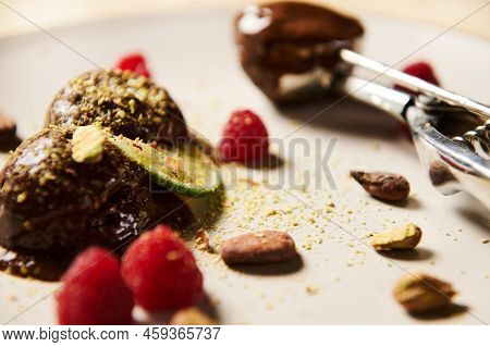Flat Lay Of Frozen Chocolate Ice Cream Balls, Garnished With Pistachios, Cocoa Beans, Raspberries An