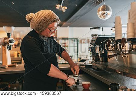 Male Barista Holding Tamper And Press Ground Coffee In Holder To Make Espresso For Client