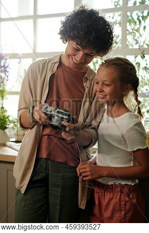 Young Smiling Woman In Casualwear Showing New Photos To Her Daughter