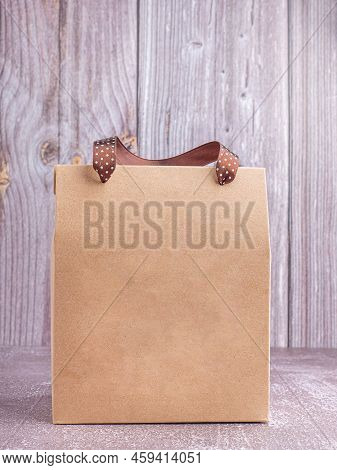 Brown Paper Bag Packaging With Ribbon Handles Placed On A Gray Stone Background With A Wooden Wall. 