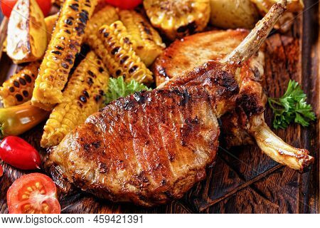 Close-up Of Bbq Tomahawk Pork Chops, Bone-in Steak With Grilled Corn Disks And Corn Ribs, Wedges Pot