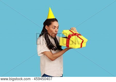 Portrait Of Surprised Woman In Yellow Party Cone Looking Into Gift Box, Opening Present And Peeking 