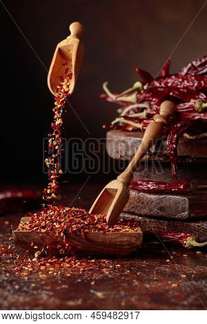 Chilli Flakes Are Poured Into A Wooden Dish. Chilli Flakes And Dried Chili Peppers On A Brown Backgr