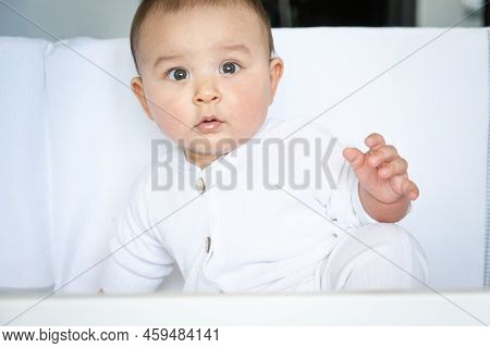 Cute Portrait Of A Baby In A Crib Close-up. A Child In White Clothes On White Underwear. Tenderness 
