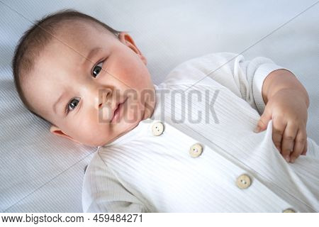 Cute Portrait Of A Baby In A Crib Close-up. A Child In White Clothes On White Underwear. Tenderness 