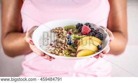 Yogurt, Blackberry Muesli, Raspberries, Blueberries, Kiwi And Peaches In A White Bowl Holding Young 