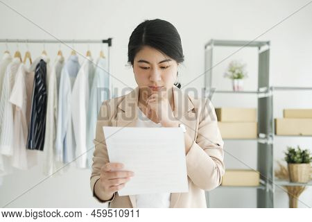 Young Asian Female Freelan Standing Reading Report On Paper In Online Clothing Store.