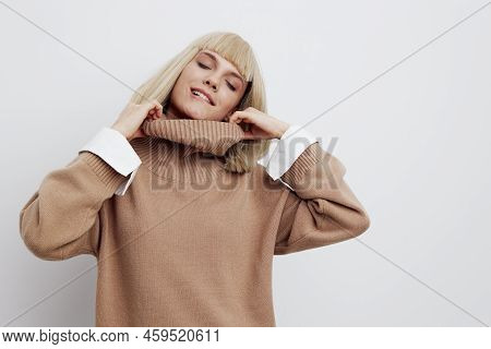 A Beautiful Happy Woman Stands On A Light Background In A Sweater And Shirt, Pulls The Neck Gently T