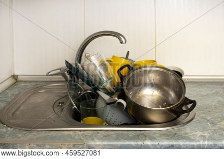 Dirty And Unwashed Dishes Are Stacked In The Kitchen Sink. Unwashed Cups, Plates, Pots, Forks And Sp