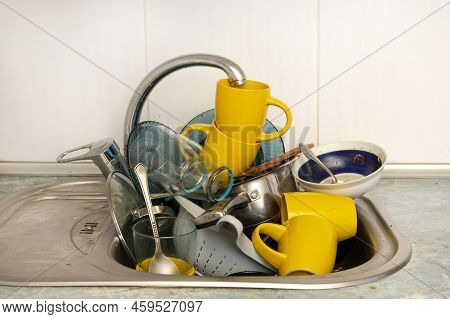 Dirty And Unwashed Dishes Are Stacked In The Kitchen Sink. Unwashed Cups, Plates, Pots, Forks And Sp